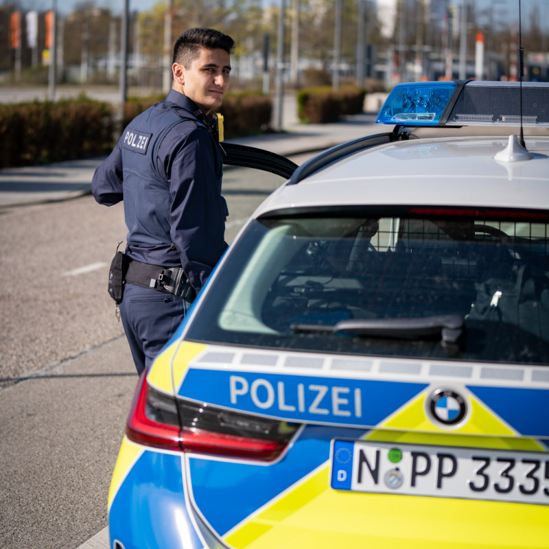 Kollege der Bayerischen Polizei mit Fahrzeug im Streifendienst.