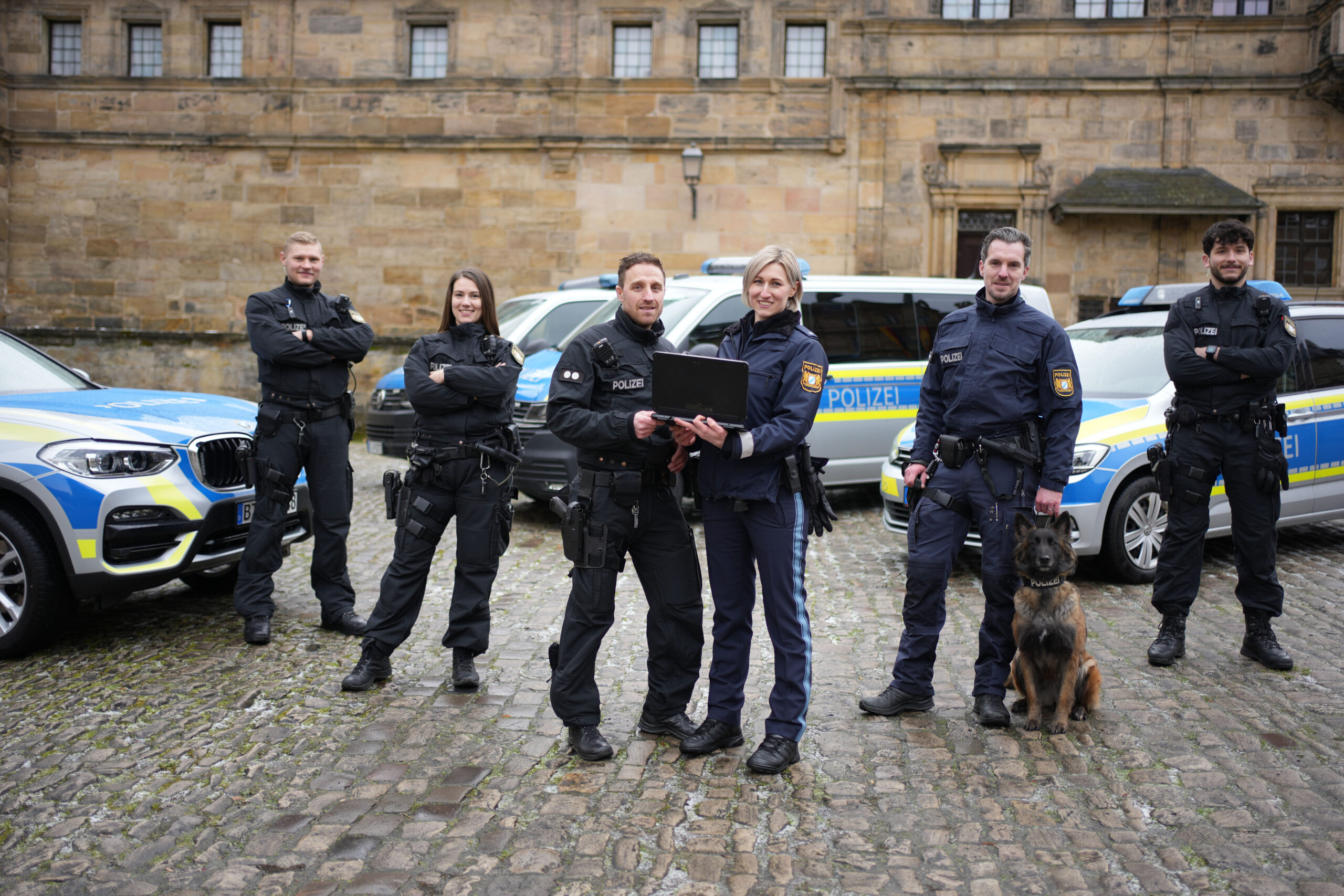 Team der Polizei Bayern mit Kolleginnen und Kollegen mit Hundestaffel und Fahrzeugen.