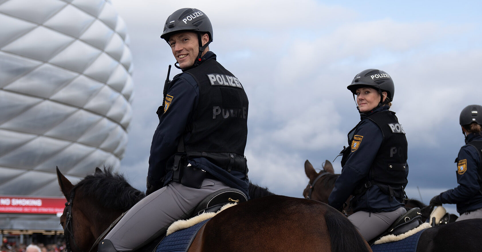 Drei Kolleginnen und Kollegen der Pferdestaffel der Bayerischen Polizei im Einsatz auf ihren Pferden am Olympiastadion in München.