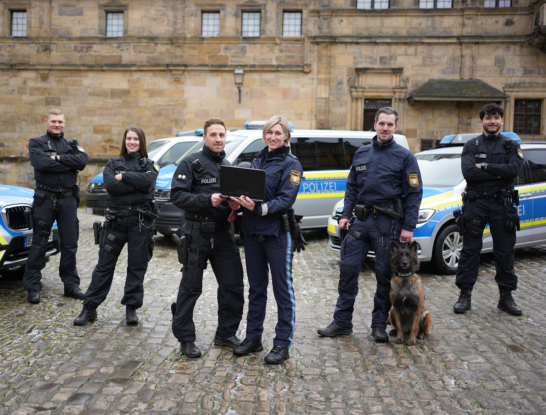 Team der Polizei Bayern mit Kolleginnen und Kollegen mit Hundestaffel und Fahrzeugen.