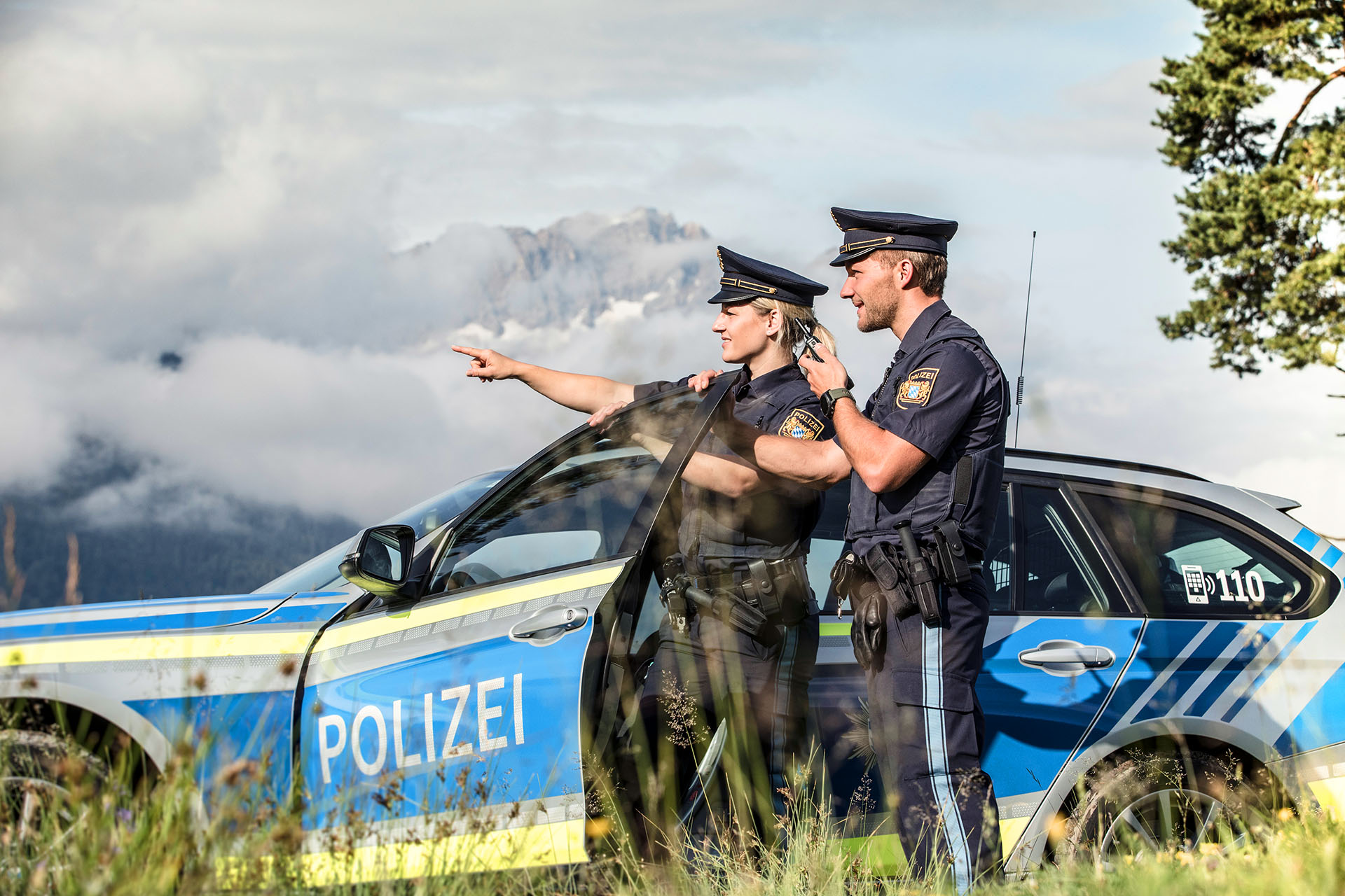 Kollegin und Kollege der Bayerischen Polizei mit Fahrzeug bei der Kontrolle